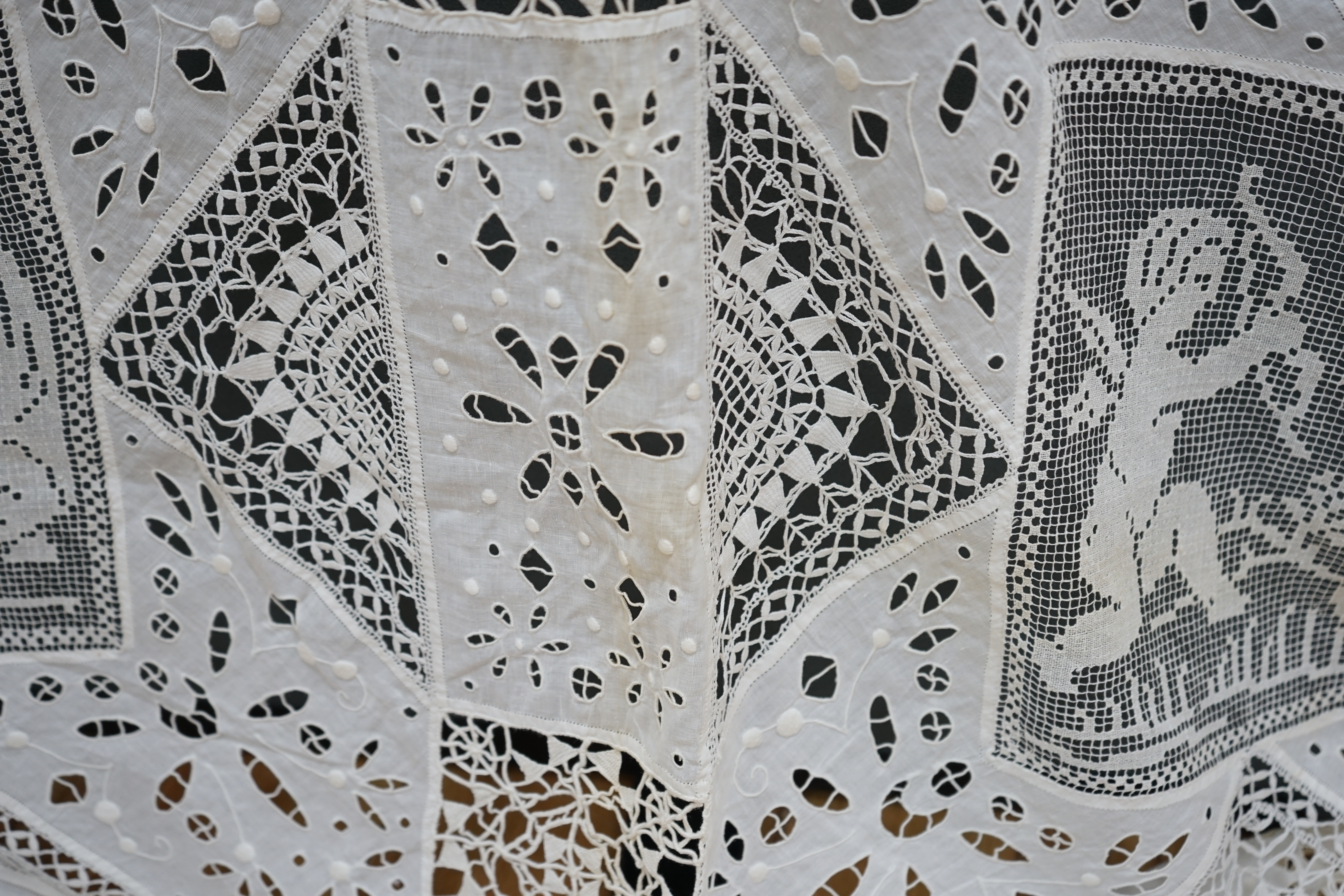 An early 20th century Italian ornate bedcover, worked with square fillet lace insertions of putti, white multi patterned cut work squares on fine linen and similar multi patterned needle lace squares, creating a unique b